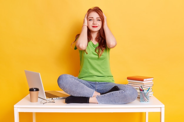 Moe meisje met hoofdpijn zittend op een bureau met gekruiste benen