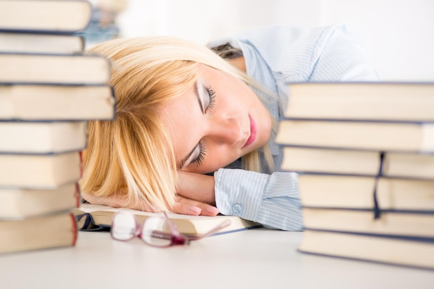 Foto moe student viel in slaap tussen vele boeken, tijdens het leren.