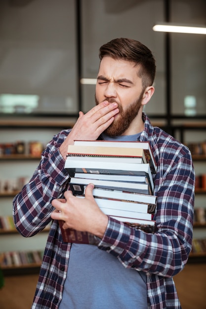 Moe uitgeput man met stapel boeken en geeuwen