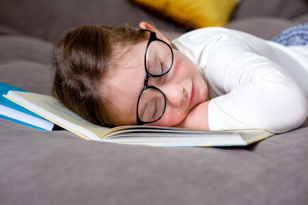 Moe van het studeren en lezen van een schattig klein meisje met een bril slaapt op het bed op een open boek