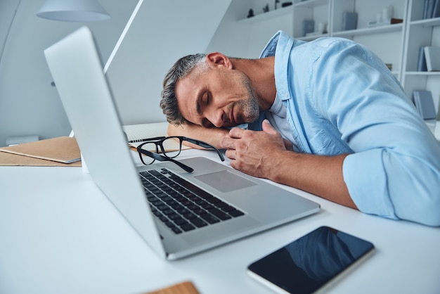 Moe volwassen man slapen terwijl hij aan het bureau zit