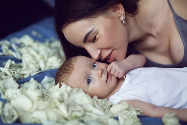Moeder brunette met een pasgeboren jongen ligt op het bed met witte rozenblaadjes