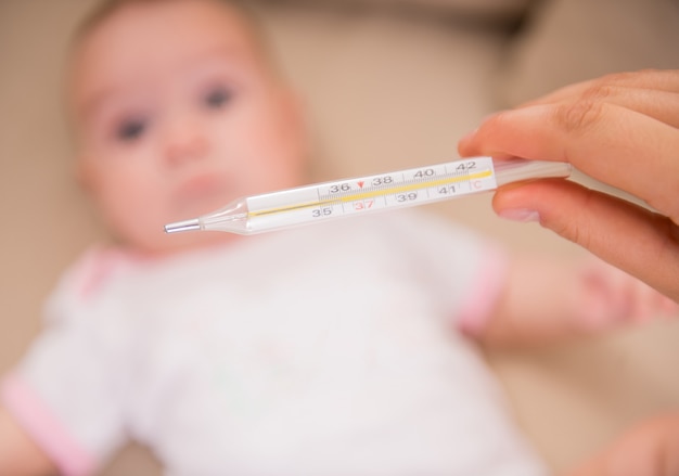 Moeder controleert de temperatuur van de zieke kleine baby.