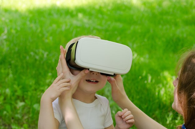 Moeder corrigeert zijn zoon bril van virtual reality tegen de muur van groen gras