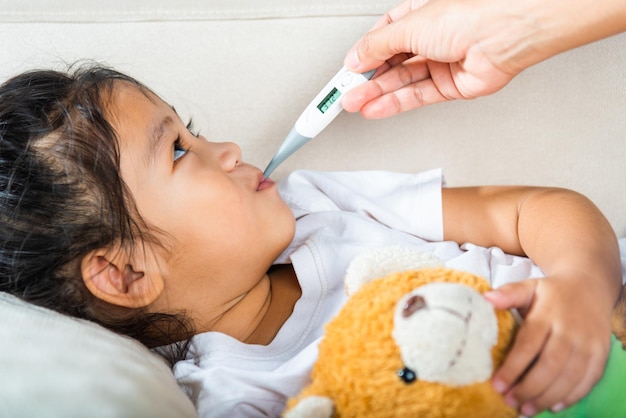 Moeder die de temperatuur van haar zieke dochter controleert met een thermometer in de mond