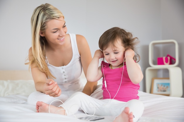 Moeder die dochter met hoofdtelefoons op bed bekijkt