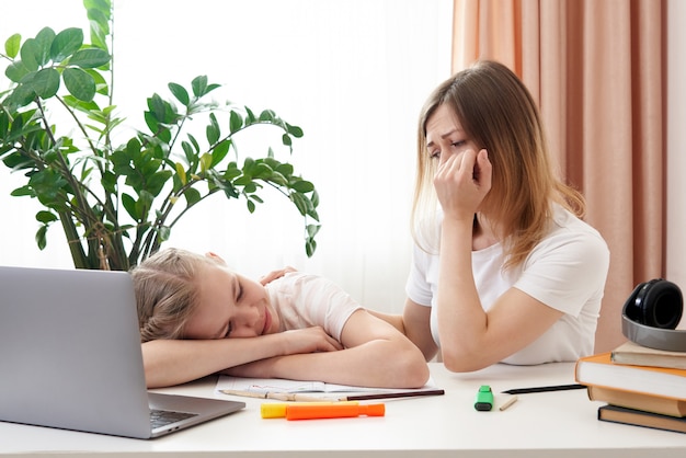 Moeder die droevige dochter helpt om huiswerk te doen. Het concept van thuisonderwijs in quarantaine. Moeilijkheden met afstandsonderwijs