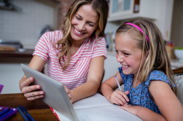 Moeder die een digitale tablet gebruikt terwijl dochter met haar huiswerk helpt