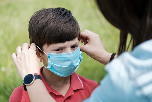 Moeder die een jonge jongen past met een gezichtsmasker