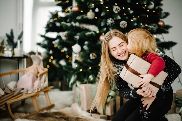 Moeder die geschenken uitwisselt met dochter Ouder en klein kind hebben plezier in de buurt van de kerstboom binnenshuis Liefdevolle familie met cadeautjes in de kamer De ochtend voor kerst Portret moeder en kind close-up