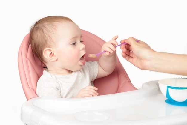 Moeder die haar leuk die babymeisje als voorzitter voedt op witte achtergrond wordt geïsoleerd.