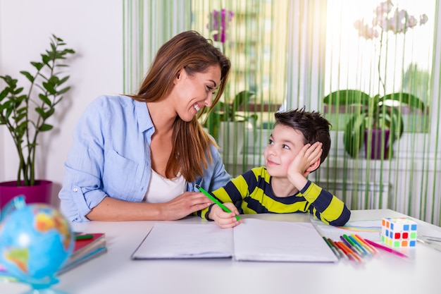 Moeder die met huiswerk helpt aan haar zoon binnen. Familie, kinderen en gelukkige mensen concept.