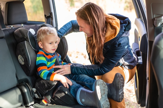 Moeder die veiligheidsgordel vastmaakt voor haar babyjongen in zijn autostoeltje. Veiligheid voor autostoeltjes voor kinderen