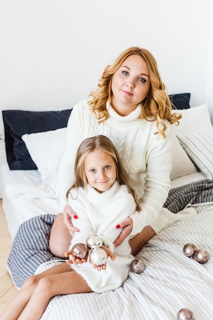 Moeder dochter blond haar witte truien liggen in bed met speelgoed voor kerstmis en nieuwjaar