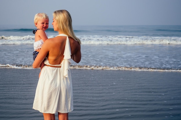 Moeder dochter plezier rusten op het strand. Familie vakantie reizen. Kaukasisch wijfje met peuterbaby bij oceaan.