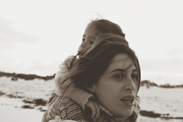 Foto moeder draagt dochter op het strand tegen de lucht