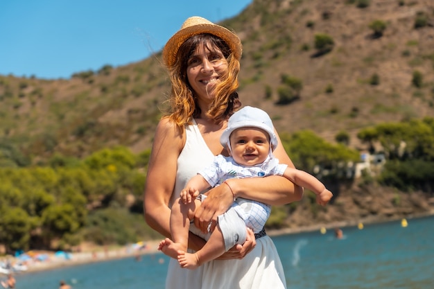Moeder draagt een hoed met haar baby op vakantie in Cala Montjoi, strand van het Parc Natural del Cap Creus, Gerona, Costa Brava van Catalonië in de Middellandse Zee. Spanje