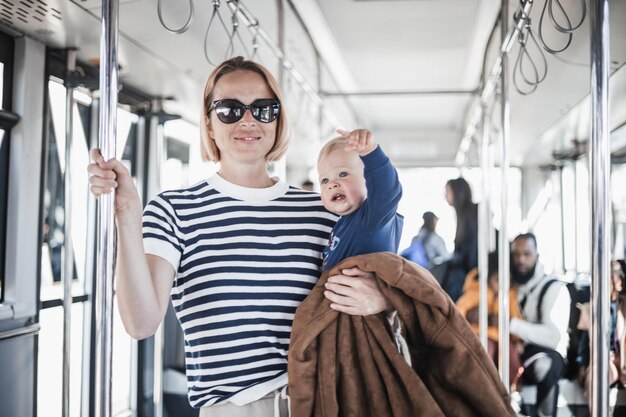 Moeder draagt haar kind terwijl ze staat en vasthoudt aan de barhouder op de bus moeder houdt baby vast