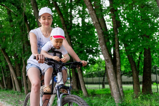 moeder draagt in de zomer een kind in een kinderstoel op een fiets in het park