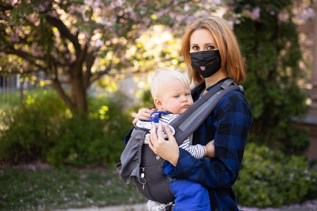 Moeder draagt masker met zoontje die in het park de sakura-boom speelt