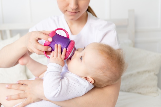 Moeder drinkt of voedt een baby op een wit bed thuis, babyvoedingconcept.