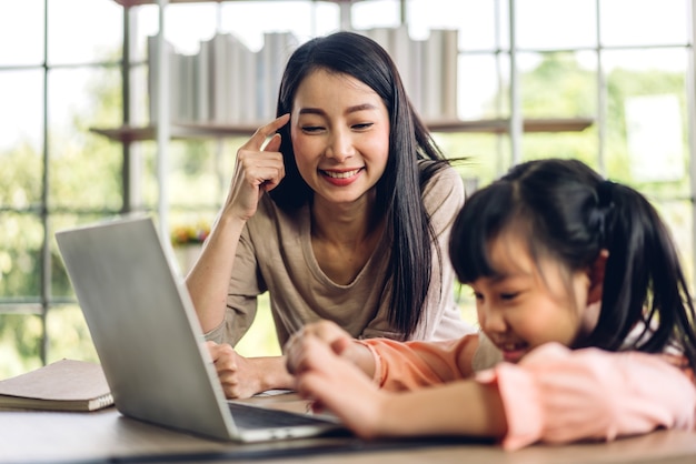 Moeder en aziatische jongen meisje leren en kijken naar laptopcomputer maken huiswerk studeren kennis met online onderwijs e-learning systeem. videoconferentie voor kinderen met leraar tutor thuis