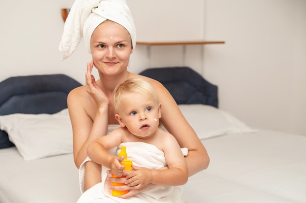 Moeder en baby baby in witte handdoeken na het baden toepassen zonnebrandcrème of na zonnebrandolie of crème