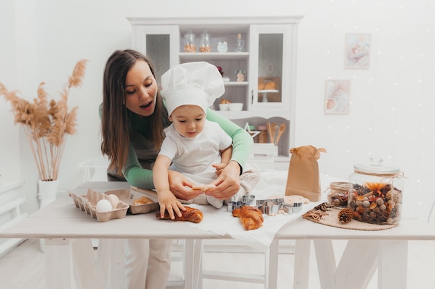 Moeder en baby bakken in de keuken. Gelukkige moeder kust haar kind, ze hebben plezier en bereiden eten. Het kind heeft een koksmuts.