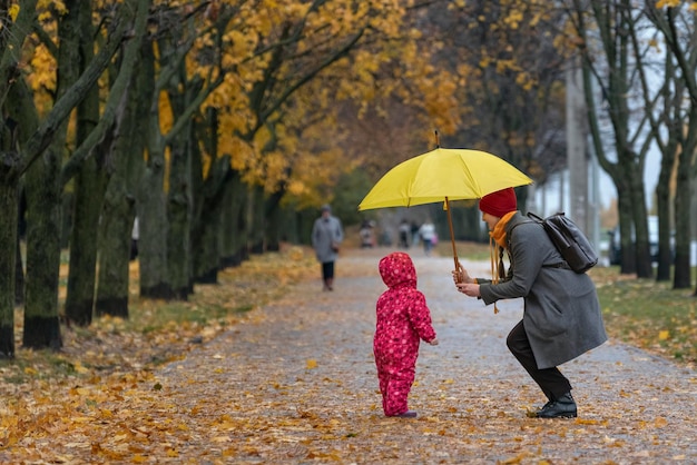 Moeder en baby in een herfstpark onder een paraplu verbergen zich voor de regen.