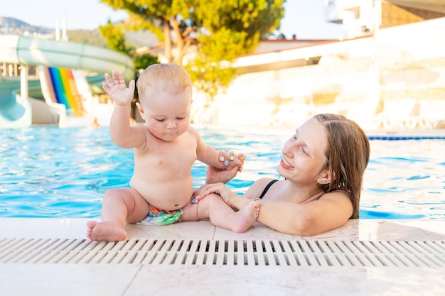 Moeder en baby in het zwembad met waterglijbanen in de zomer veel plezier met zwemmen, ontspannen en tijd doorbrengen met het gezin op vakantie