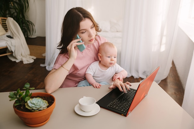 Moeder en baby in kantoor aan huis met laptop en telefoon