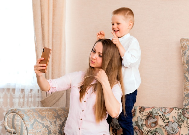 Moeder en baby nemen een selfie in een gezellige woonkamer. moeder en zoon trekken grappige gezichten en nemen foto's van zichzelf op camera