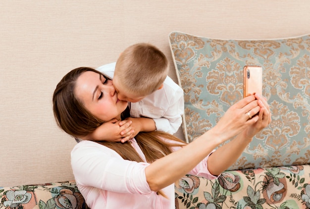 Moeder en baby nemen een selfie in een gezellige woonkamer. moeder en zoon trekken grappige gezichten en nemen foto's van zichzelf op camera