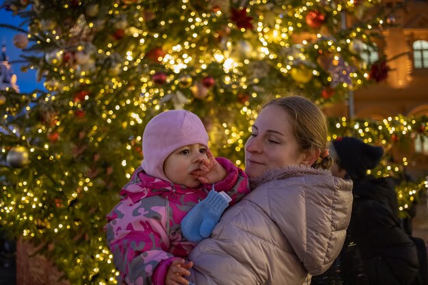 Moeder en baby op kerstmarkt in de buurt van heldere kerstboom
