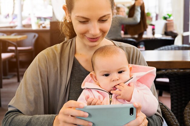 Moeder en baby outddors in een restaurant kijken naar kartons, selfie maken