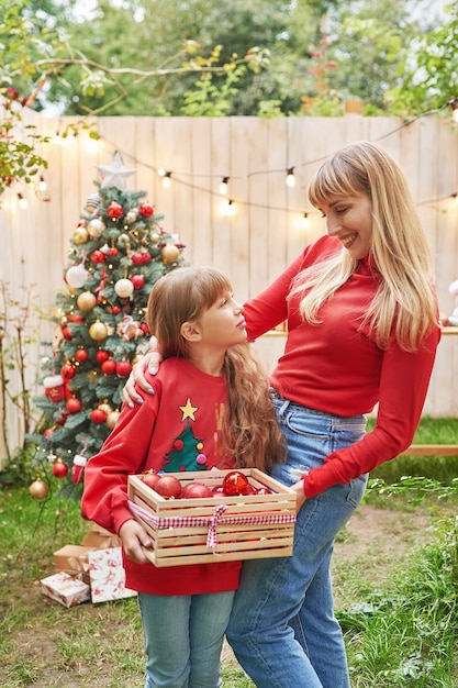 Moeder en babydochter dichtbij kerstboom met giften, familiekerstmis in juli. Wintervakantie en mensen concept. Prettige kerstdagen en gelukkig vakantie wenskaart.