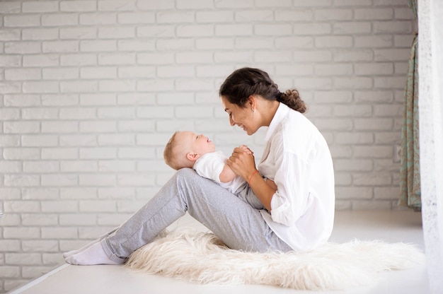 Moeder en babyjongen in luier spelen in zonnige slaapkamer. Familie samen plezier.