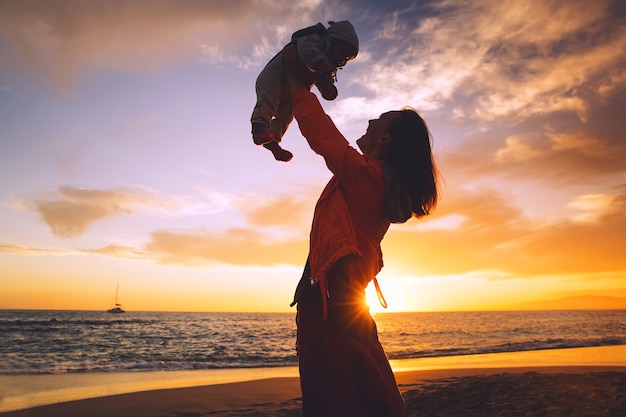 Moeder en babysilhouetten bij zonsondergang op de strandoceaan in de zomer Gelukkige familieachtergrond