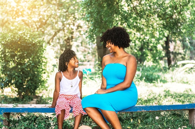 Moeder en dochter Afro-Amerikaanse etniciteit zitten in een park naar elkaar te kijken en te praten