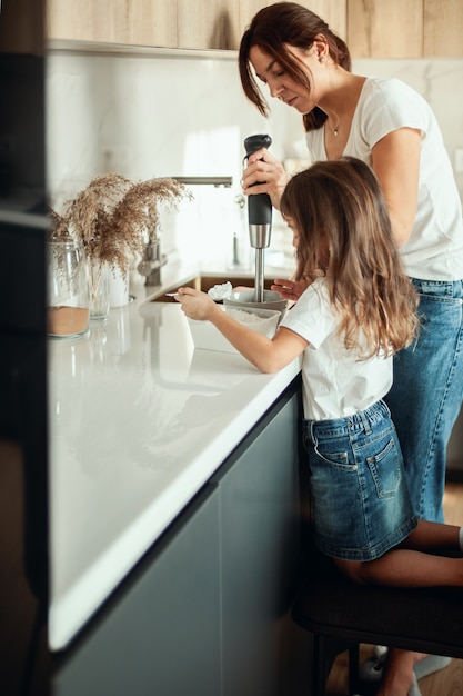 Moeder en dochter bereiden suikerglazuur voor peperkoek in hun huiskeuken. Klop met een blender. Het meisje