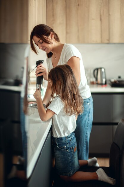 Moeder en dochter bereiden suikerglazuur voor peperkoek in hun huiskeuken. Klop met een blender. Het meisje