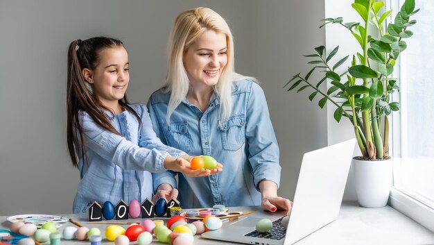 moeder en dochter bloggers met konijnenoren hoofdband om thuis in de keuken te zitten. Pasen voorbereiding eieren samen kleuren.