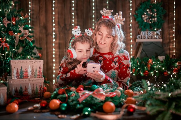 Moeder en dochter die de telefoon naast de kerstboom kijken en online winkelen.