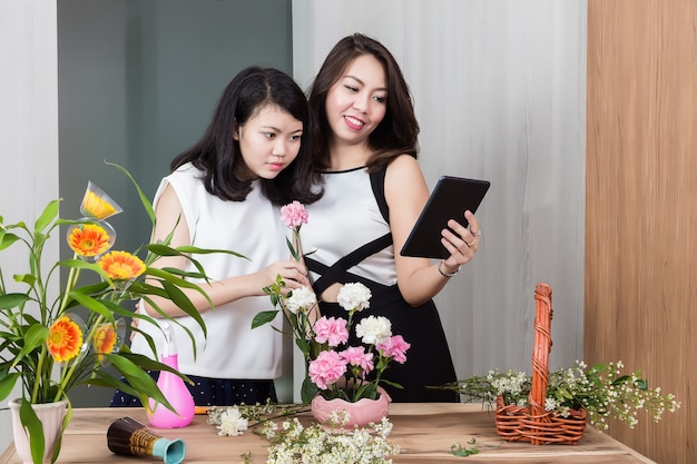 Moeder en dochter die digitale tablet gebruiken terwijl het schikken van bloemen op houten lijst