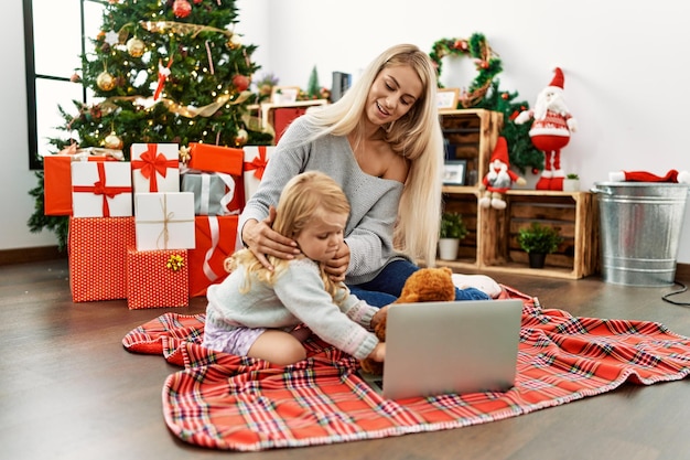 Moeder en dochter die laptop gebruiken die thuis bij de kerstboom zitten