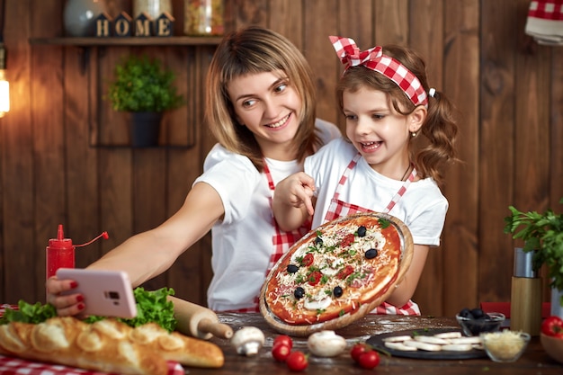 Moeder en dochter die selfie met pizza op smartphone nemen