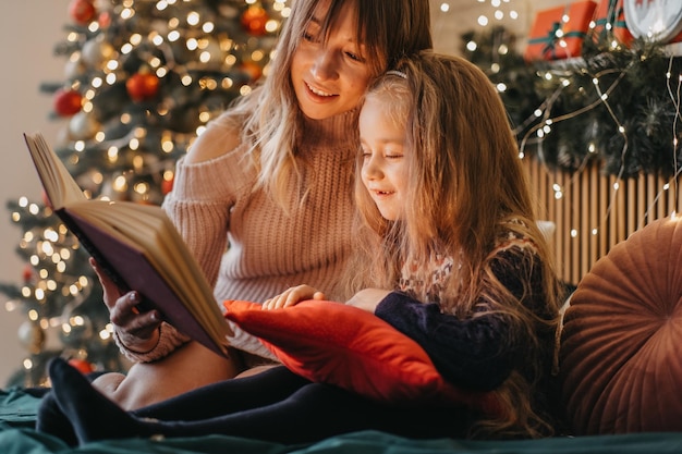 Moeder en dochter die sprookjes lezen tijdens kerstavond, geweldige sfeer van liefde en vertrouwen, geloof in wonderen, fijne feestdagen