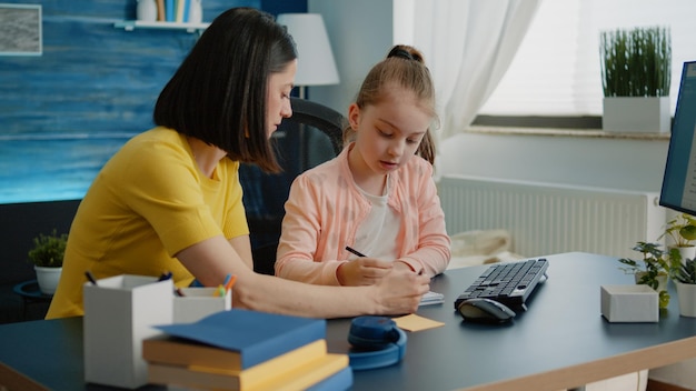 Moeder en dochter doen samen huiswerk voor online les in een klaslokaal op afstand. Ouder die meisje helpt met schoolwerk en taken voor afstandsonderwijs op de computer thuis.