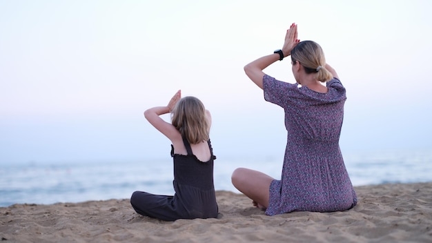 Moeder en dochter doen yoga mediteren in lotushouding op het strand