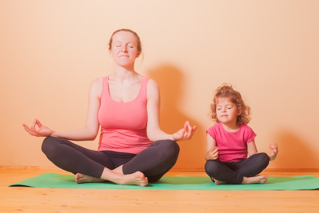 Moeder en dochter doen yoga-oefeningen op groen tapijt